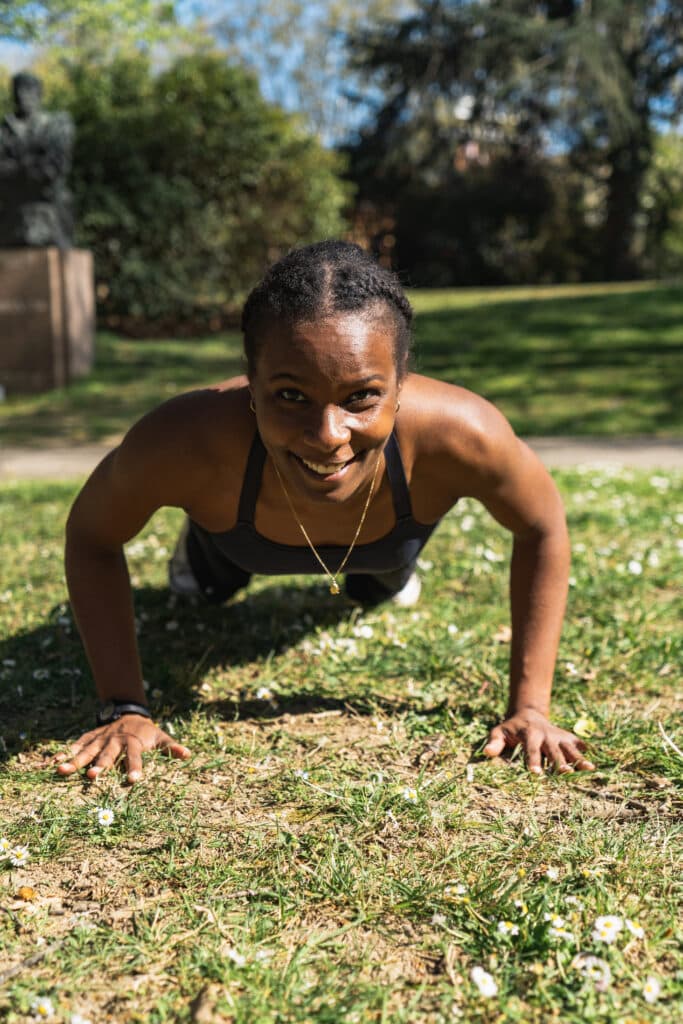 Coach sportive souriante en pleine séance de pompes sur l’herbe, en extérieur à Toulouse – évaluation de la condition physique et accompagnement personnalisé.