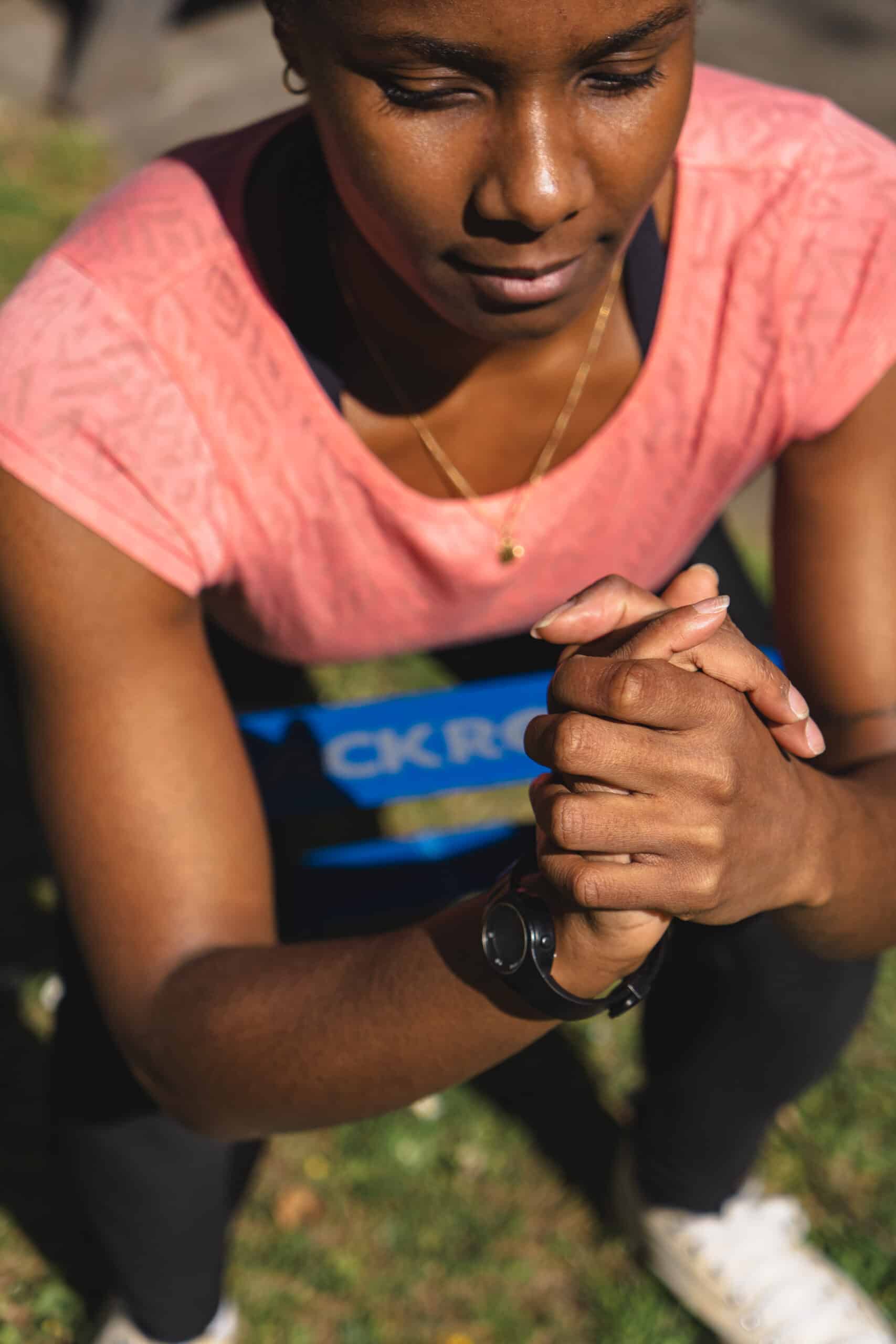 Femme en tenue de sport effectuant un exercice de gainage en extérieur, concentrée, mains jointes, portant une montre connectée – coaching sportif à domicile.