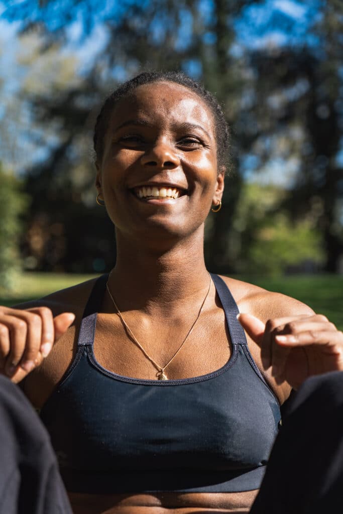 Coach sportive souriante en plein entraînement en extérieur, vêtue d’une brassière de sport noire – séance de fitness et bien-être au soleil.
