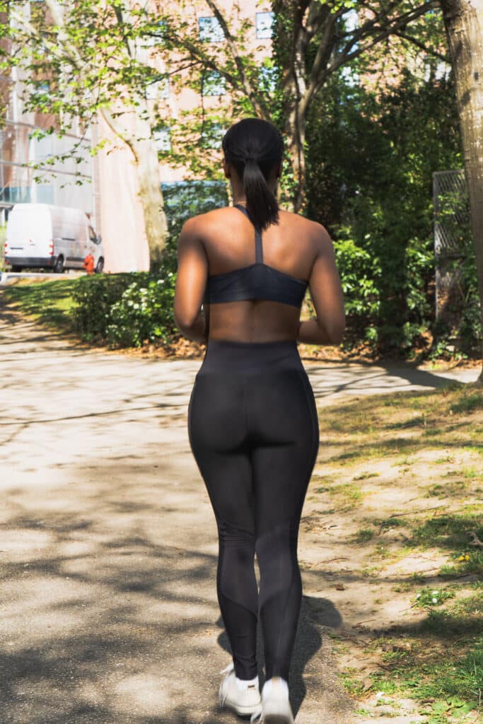 Femme en tenue de sport marchant dans un parc urbain, vue de dos – échauffement ou marche d’observation pour bilan forme personnalisé à Toulouse.