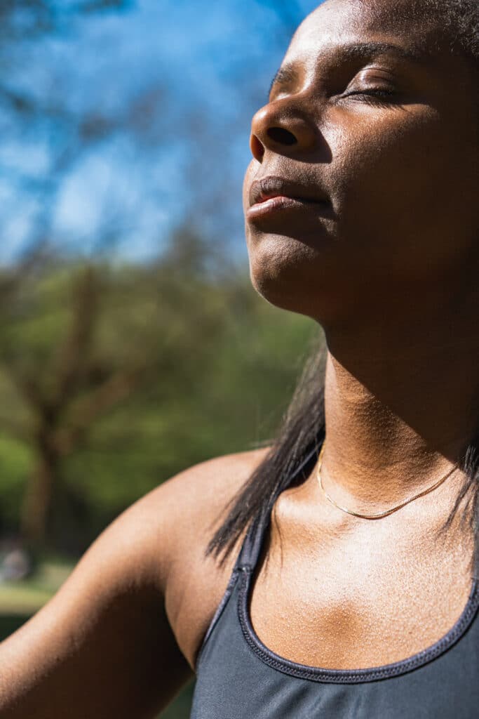 Femme les yeux fermés en pleine séance de respiration ou de méditation en extérieur, captant la lumière du soleil – bien-être et recentrage mental.