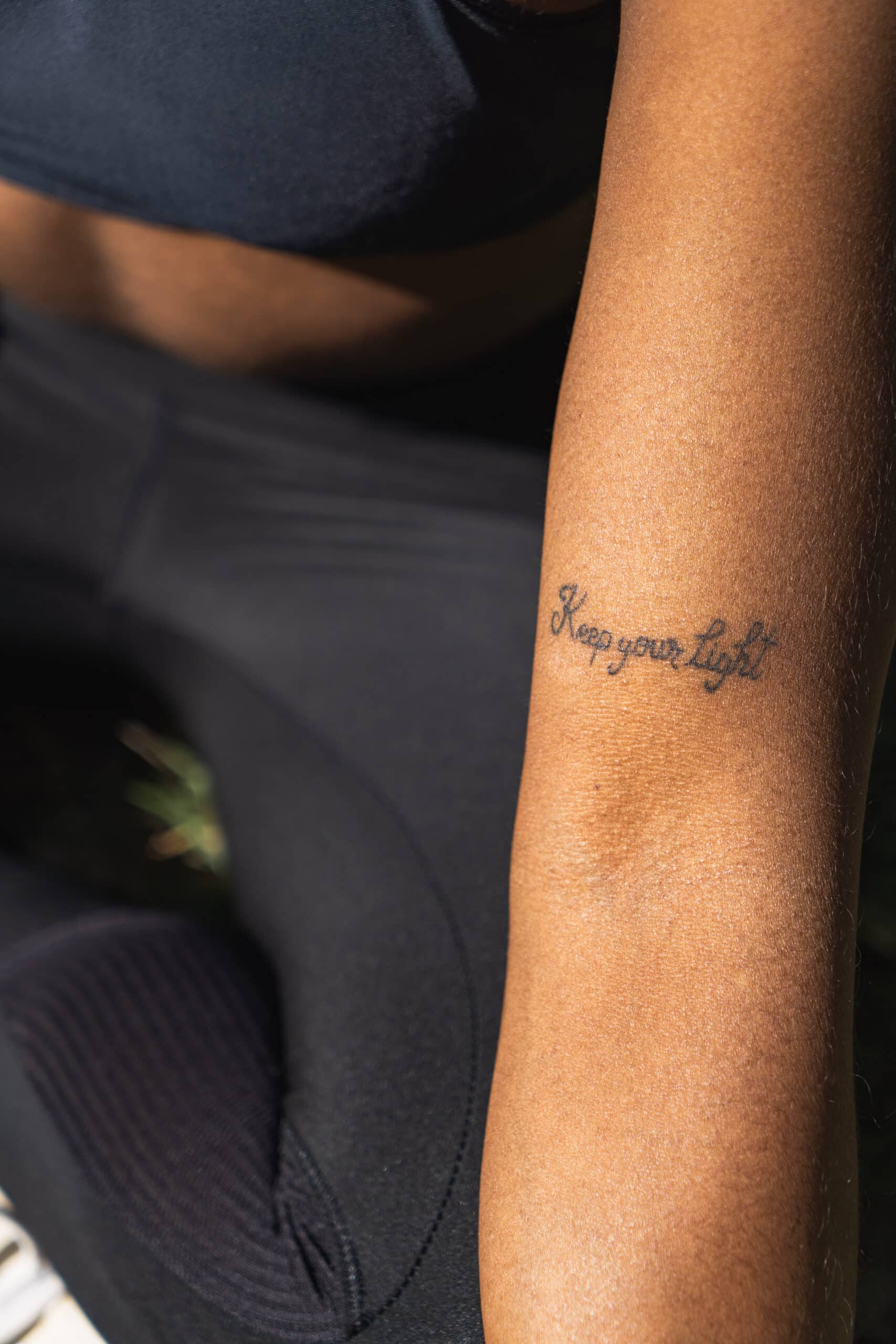 Tout savoir sur l’hypnose PNL Tatouage "Keep your light" sur l’avant-bras d’une femme en tenue de sport, assise au soleil – message de motivation et de développement personnel.